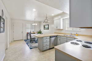 Kitchen featuring a sink, a textured ceiling, a chandelier, dishwasher, and a peninsula