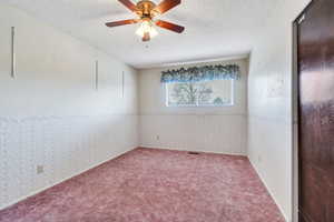 Spare room featuring wallpapered walls, a textured ceiling, ceiling fan, and wainscoting