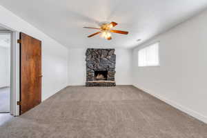 Unfurnished living room with baseboards, a ceiling fan, a stone fireplace, and carpet