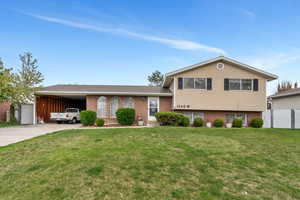 Tri-level home with a front lawn, fence, driveway, and an attached carport