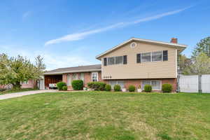 Tri-level home with a chimney, driveway, an attached garage, fence, and a front yard