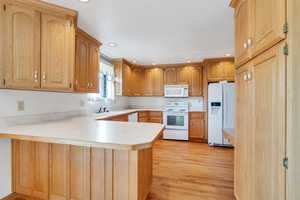 Kitchen with light wood finished floors, a peninsula, recessed lighting, white appliances, and light countertops