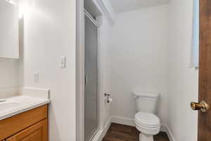 Full bath featuring a stall shower, toilet, baseboards, wood finished floors, and vanity