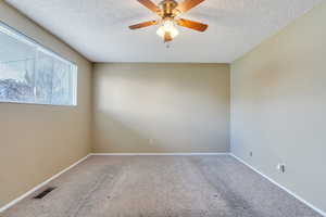Carpeted spare room with baseboards, visible vents, a textured ceiling, and ceiling fan
