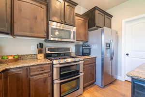 Kitchen with light stone counters, baseboards, appliances with stainless steel finishes, and light wood-style floors