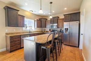 Kitchen with light stone counters, a sink, dark brown cabinetry, light wood-style flooring, and appliances with stainless steel finishes