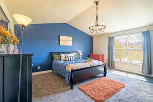 Bedroom with vaulted ceiling, carpet flooring, baseboards, and a notable chandelier