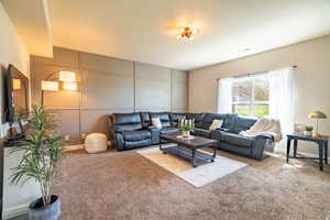 Carpeted living area featuring a decorative wall and visible vents