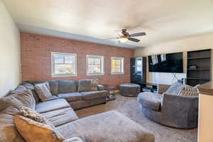 Carpeted living area featuring brick wall and a ceiling fan