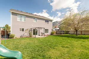 Back of house with a fenced backyard, a pergola, a playground, a patio area, and a yard