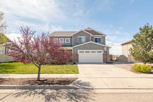 View of front of property featuring a front lawn, driveway, stone siding, fence, and a garage