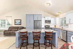 Kitchen featuring high vaulted ceiling, a center island, a sink, light wood finished floors, and appliances with stainless steel finishes