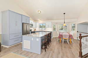 Kitchen featuring light wood-style floors, vaulted ceiling, appliances with stainless steel finishes, and a sink