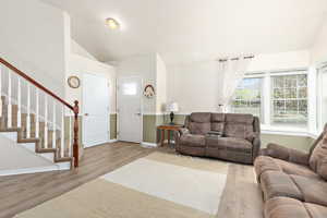 Living area featuring vaulted ceiling, wood finished floors, baseboards, and stairway