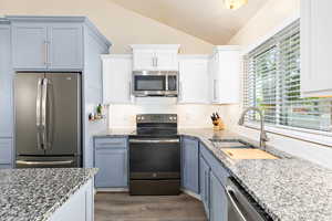 Kitchen featuring lofted ceiling, light stone counters, stainless steel appliances, and a sink
