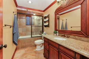 Bathroom with toilet, stone finish floor, vanity, tiled shower / bath, and ornamental molding