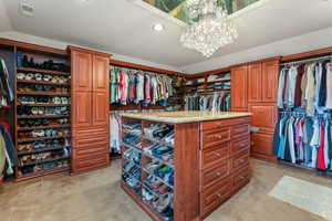 Primary Walk in closet with light colored carpet, a notable chandelier. Laundry and Fridge included.