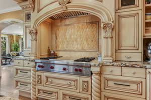 Kitchen featuring stainless steel gas stovetop, light stone counters, arched walkways, crown molding, and glass insert cabinets