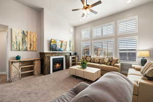 Carpeted living area featuring a warm lit fireplace, ceiling fan, a towering ceiling, baseboards, and recessed lighting