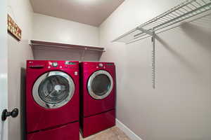 Laundry area with tile patterned floors, a textured ceiling, washer and clothes dryer, baseboards, and laundry area
