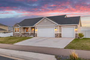 View of front of property with stone siding, a lawn, fence, and a garage