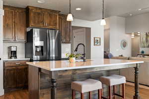 Kitchen with a breakfast bar, a kitchen island with sink, stainless steel fridge with ice dispenser, light countertops, and dark wood-style flooring