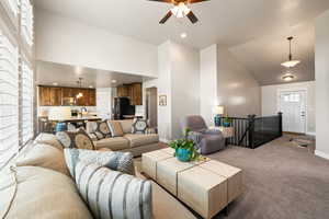 Carpeted living room with a ceiling fan, baseboards, high vaulted ceiling, and a sink