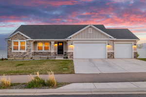 View of front of house with a yard, stone siding, concrete driveway, and a garage