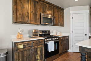 Kitchen featuring stainless steel appliances, light countertops, dark brown cabinetry, and dark wood-type flooring