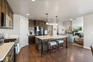 Kitchen featuring dark wood finished floors, dark brown cabinets, open floor plan, a kitchen bar, and appliances with stainless steel finishes