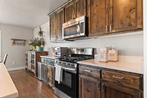 Kitchen with stainless steel appliances, light countertops, dark brown cabinetry, and dark wood finished floors