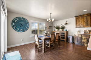 Dining room featuring a textured ceiling, dark wood-style flooring, visible vents, baseboards, and an inviting chandelier
