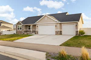 Craftsman-style home with driveway, stone siding, fence, an attached garage, and a front yard