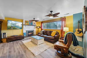 Living area featuring light wood-style flooring, visible vents, a ceiling fan, and a stone fireplace