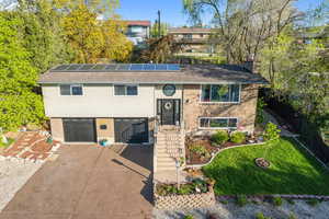 Bi-level home with concrete driveway, a carport, an attached garage, roof mounted solar panels, and brick siding