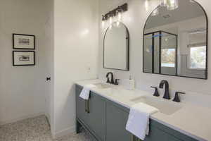 Bathroom featuring baseboards, a sink, a shower stall, and double vanity