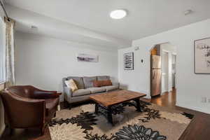 Living room with arched walkways, wood finished floors, visible vents, and baseboards