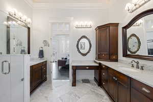 Bathroom featuring two vanities, ornamental molding, marble finish flooring, baseboards, and connected bathroom