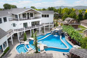 Rear view of house featuring a balcony, a mountain view, a pool with connected hot tub, a shingled roof, and a residential view