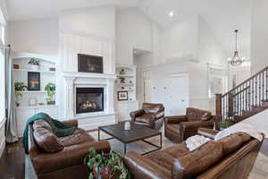 Living area with a glass covered fireplace, a chandelier, high vaulted ceiling, healthy amount of natural light, and wood finished floors