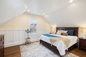Bedroom featuring wood-type flooring, lofted ceiling, a wainscoted wall, and a decorative wall