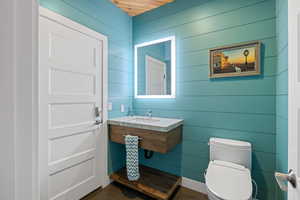 Half bathroom featuring toilet, a sink, tile patterned floors, and wood walls
