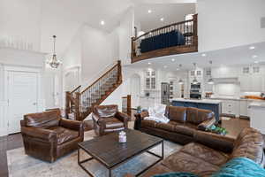 Living room with a towering ceiling, stairway, wood finished floors, a chandelier, and recessed lighting