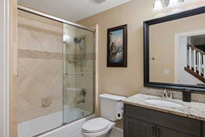 Full bath with vanity, toilet, and shower / bath combination with glass door