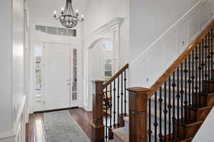 Entryway featuring a decorative wall, arched walkways, a chandelier, dark wood-style flooring, and stairway