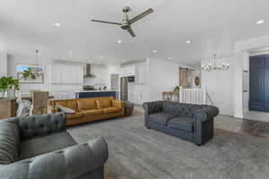 Living area with ceiling fan with notable chandelier, wood finished floors, recessed lighting, and a barn door