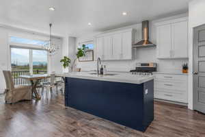 Kitchen featuring a sink, a kitchen island with sink, light countertops, wall chimney exhaust hood, and stainless steel range with gas stovetop