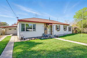 View of front of property featuring a carport, concrete driveway, a front lawn, and a garage