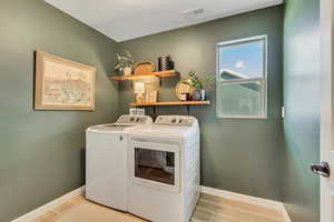 Clothes washing area with baseboards, washer and clothes dryer, laundry area, and light wood-style floors