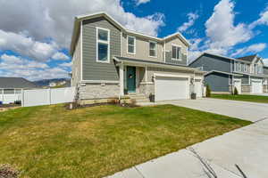 View of front facade featuring driveway, stone siding, board and batten siding, an attached garage, and fence